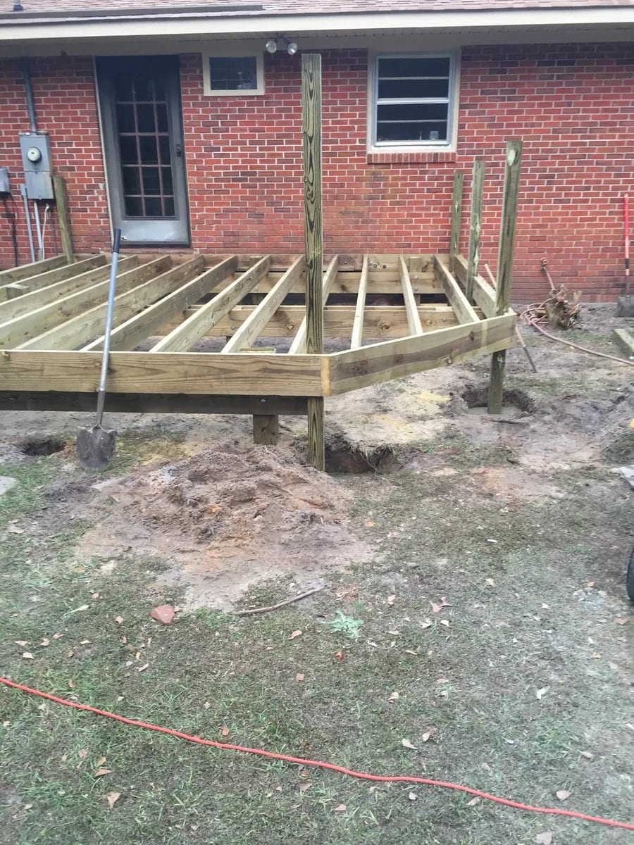 Wood deck framing and joists beside a brick home
